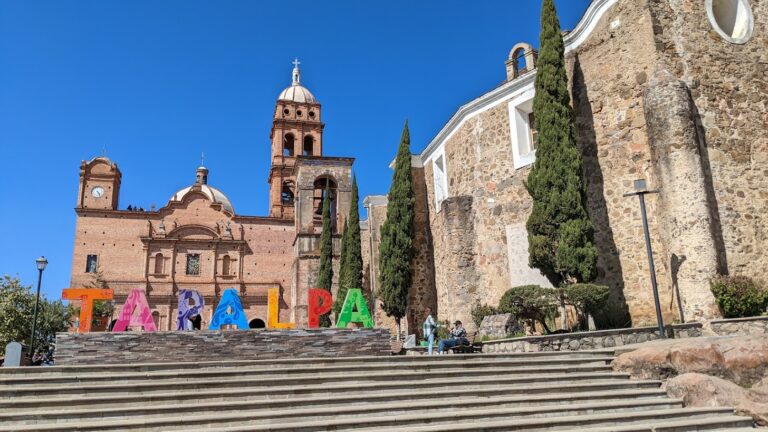 A set of stairs leading to a sign of individual letters reading "TAPALPA." Beyond that are two churches.