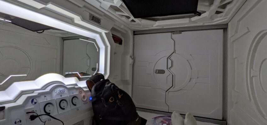 A sleeping pod with mirror on the side and door at the far end