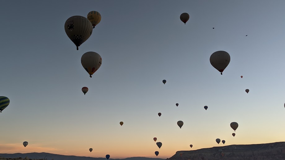 Many hot air balloons silhouetted against the sky just before sunrise
