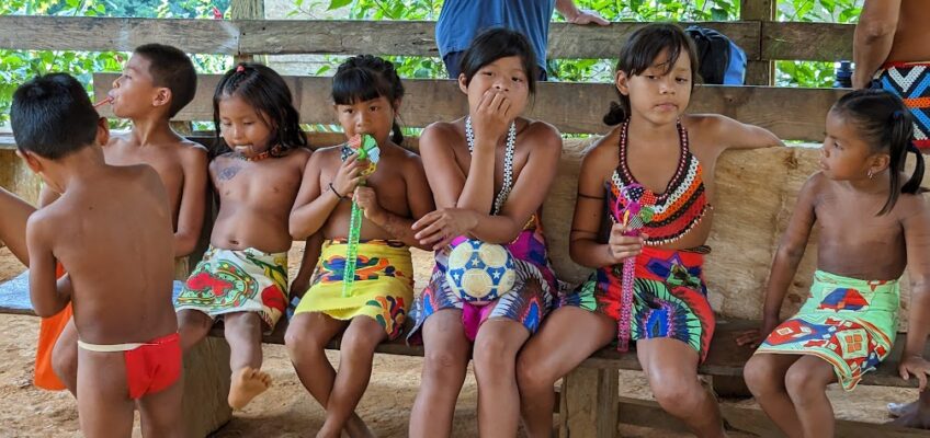 A group of indigenous children sitting on a bench wearing traditional costumes