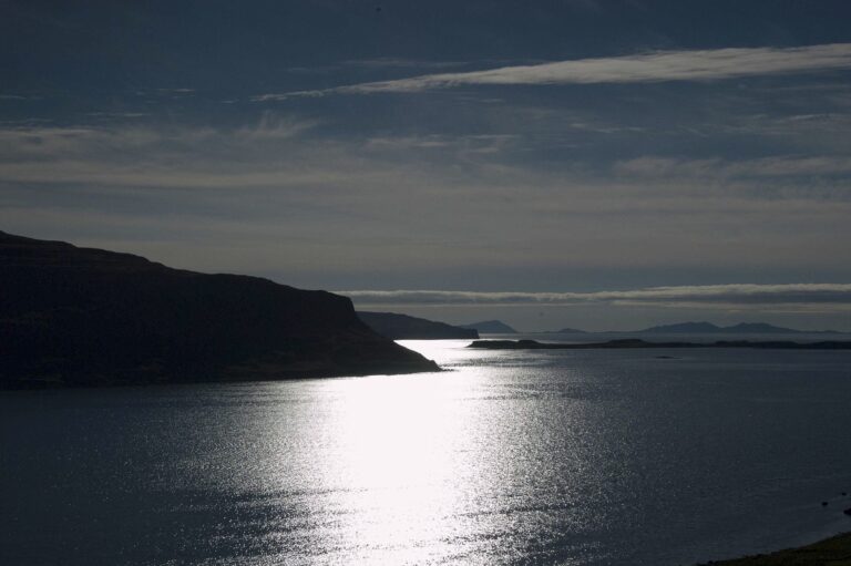 reflection of moonlight on calm water with an island and a mostly dark sky